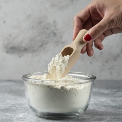 Woman hand holding spoon on top of flour bowl. High quality photo